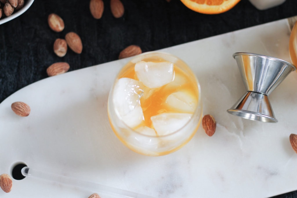Marble cutting board with a clear glass of Bourbon Cocktail surrounded by almonds and citrus