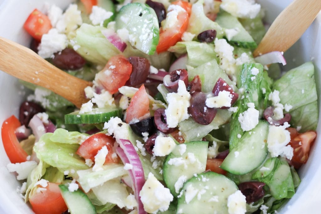 Large white ceramic bowl of Greek salad with wooden salad servers. 