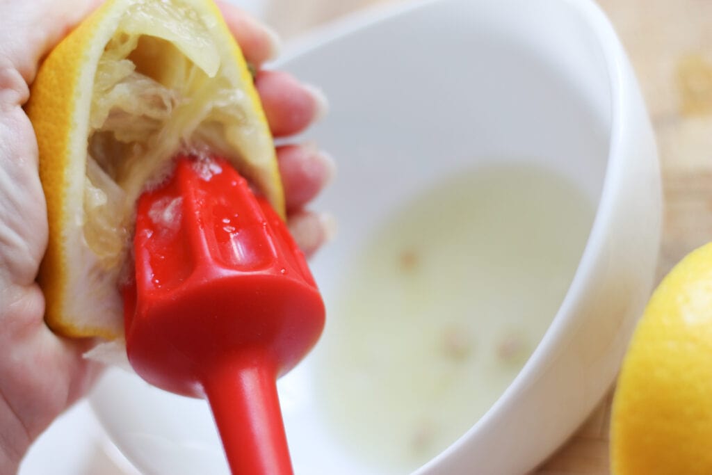 lemon being juiced into a white bowl.