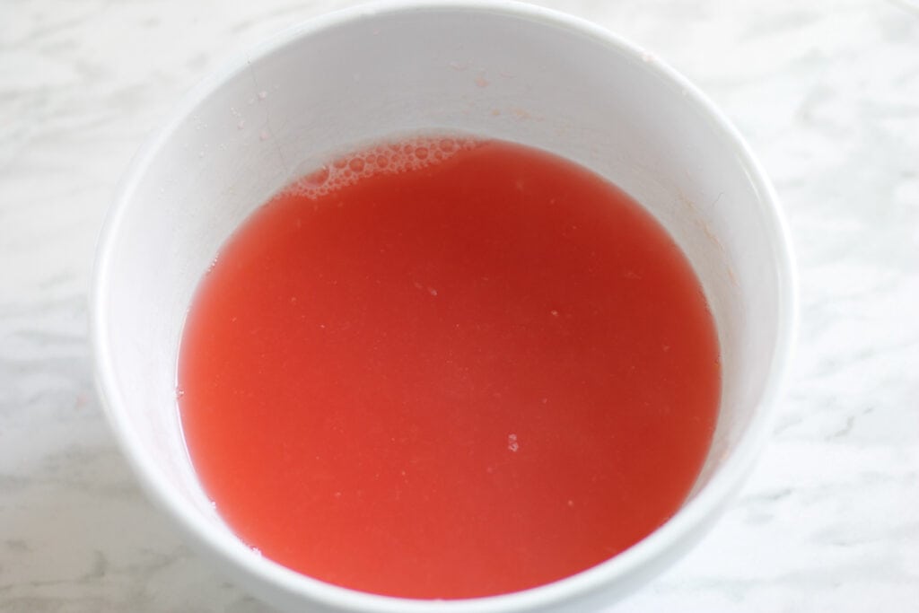 White bowl with bright pink rhubarb concentrate in it.