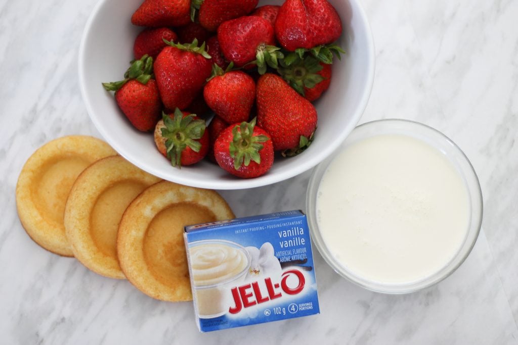 Ingredients needed to make cake arranged around a white ceramic bowl filled with fresh strawberries.