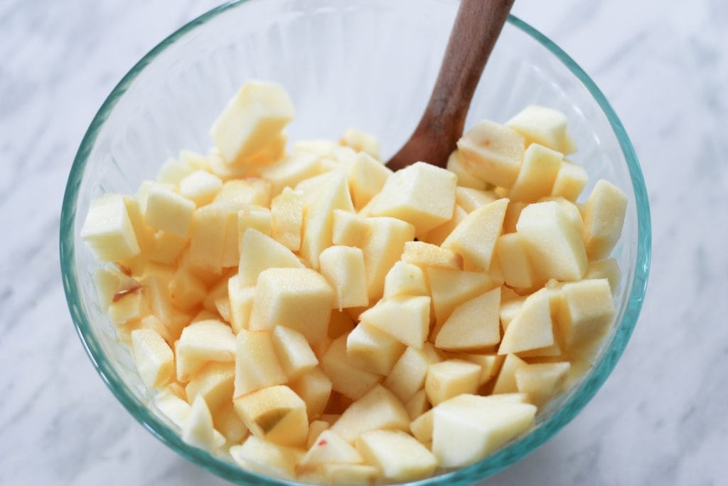 Glass bowl filled with chopped apples and a wooden spoon.