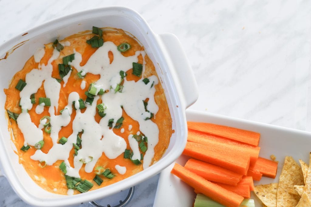 White ceramic dish with dip surrounded by carrot sticks and tortilla chips.
