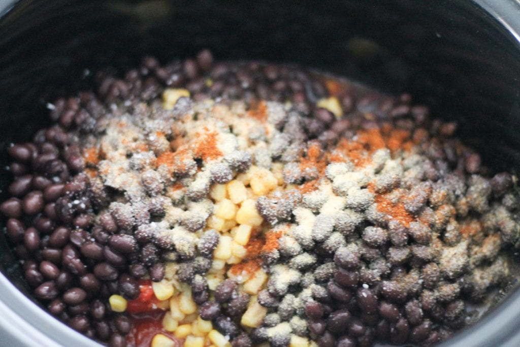 Slow cooker with ingredients for soup- beans and spices on top.